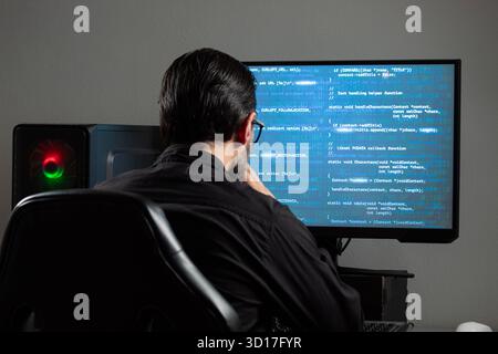 Nahaufnahme eines Mannes, der rückwärts einen Computerbildschirm mit einem blauen HTML-Code auf dem Bildschirm beobachtet Stockfoto