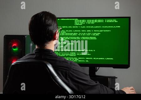 Nahaufnahme eines Mannes, der rückwärts einen Computermonitor mit einem grünen HTML-Programmiercode auf dem Bildschirm beobachtet Stockfoto