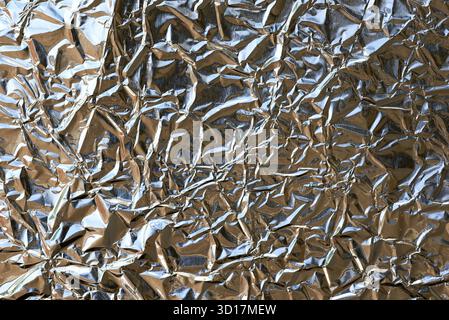 Die Nahansicht zeigt eine zerknitterte Oberfläche aus Aluminiumfolie, die Licht reflektiert und faszinierende Muster erzeugt. Diese zerknitterte Textur verleiht Tiefe und Dimension Stockfoto