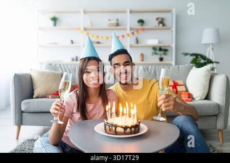 Ein Paar feiert Geburtstagsfeier mit Kuchen und Getränken in einem gemütlichen Wohnzimmer mit festlichen Artikeln Stockfoto