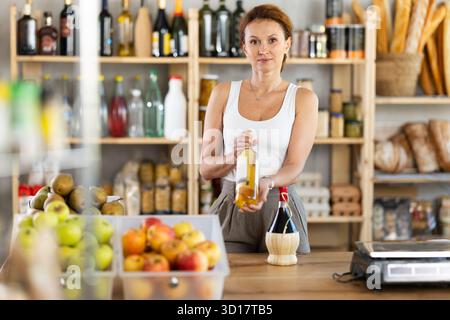 Die Verkäuferin für Erwachsene bietet Wein im Lebensmittelgeschäft an Stockfoto
