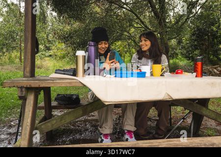 Zwei Freunde genießen ein Picknick an einem Holztisch in der Natur, entspannen und verbinden Stockfoto