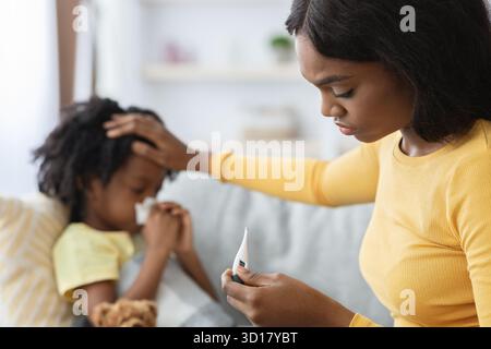 Mutter überprüft die Temperatur eines kranken Kindes während der Pflege zu Hause während der kalten Jahreszeit Stockfoto