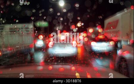 Verkehrsstau an der Kreuzung mit roten Rücklichtern von Lastwagen und Autos, gesehen durch verschwommene Regenstellen auf der Windschutzscheibe des Autos am frühen Morgen Sydney, Australien Stockfoto
