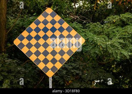 Ein gelb-schwarz kariertes Schild, das vor einer physischen Gefahr wie Straßenende, scharfe Kurven oder Sackgasse warnt Stockfoto