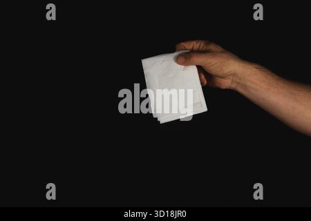 Eine Hand reicht aus, um einen Stapel weißer Servietten vor einem dunklen Hintergrund zu halten. Der Fokus liegt auf den Servietten und der Hand, wodurch ein einfaches und dennoch streifenförmiges Design entsteht Stockfoto