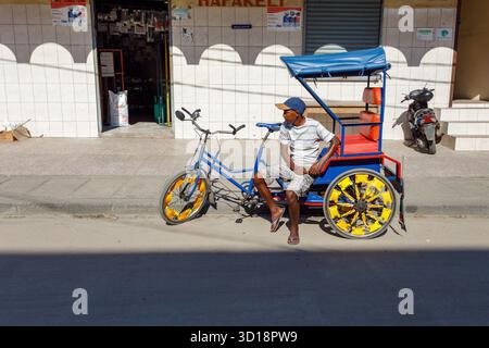 Toamasina, Madagaskar - 17. Oktober 2016: Ein ortsansässiger Taxifahrer ruht auf seinem Cyclo-pousse, einem gemeinsamen Verkehrsträger, vor einem kleinen Geschäft in Tamata Stockfoto