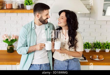 Ein lächelndes Paar mit Kaffeetassen genießen ein gemütliches Frühstück in der gemütlichen Küche Stockfoto