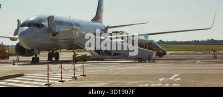 Dieses Bild zeigt ein kommerzielles Flugzeug, das auf dem Vorfeld eines Flughafens geparkt ist. Die Einstiegstreppe des Flugzeugs ist verlängert und wartet auf Passagiere Stockfoto