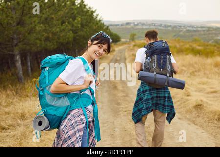 Ein paar junge, glückliche Touristen, die mit Rucksäcken auf dem Weg durch Kiefernwald spazieren gehen Stockfoto