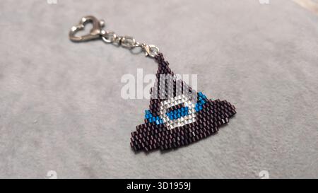 Ein Schlüsselanhänger in Form eines Zeichentrickfiguren, handgefertigt aus mehrfarbigen Perlen und Glasperlen auf grauem Hintergrund. Produktvorführung. Stockfoto