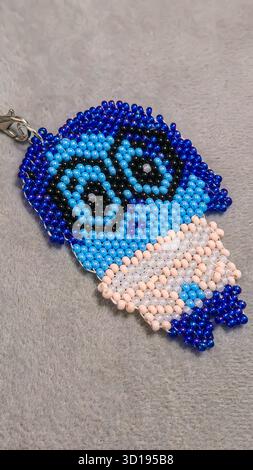 Ein Schlüsselanhänger in Form eines Zeichentrickfiguren, handgefertigt aus mehrfarbigen Perlen und Glasperlen auf grauem Hintergrund. Produktvorführung. Stockfoto