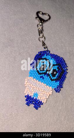 Ein Schlüsselanhänger in Form eines Zeichentrickfiguren, handgefertigt aus mehrfarbigen Perlen und Glasperlen auf grauem Hintergrund. Produktvorführung. Stockfoto