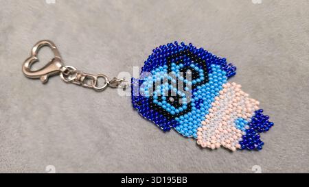 Ein Schlüsselanhänger in Form eines Zeichentrickfiguren, handgefertigt aus mehrfarbigen Perlen und Glasperlen auf grauem Hintergrund. Produktvorführung. Stockfoto
