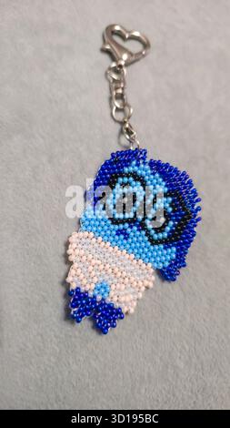 Ein Schlüsselanhänger in Form eines Zeichentrickfiguren, handgefertigt aus mehrfarbigen Perlen und Glasperlen auf grauem Hintergrund. Produktvorführung. Stockfoto