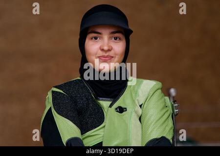 Porträt einer jungen muslimischen Frau mit Hijab und Schießausrüstung, Blick auf die Kamera, Aufnahme im Studio, selbstbewusste Athletin, Entschlossenheit Stockfoto