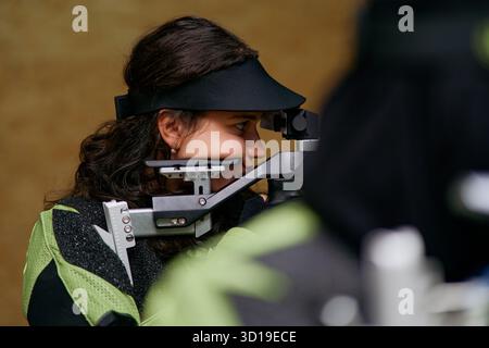 Fokussierte junge Frau, die im Schießwettbewerb mit Gewehr zielt, Präzision und Können demonstriert, Indoor-Setting, Wettkampfsport, Zielübungen Stockfoto