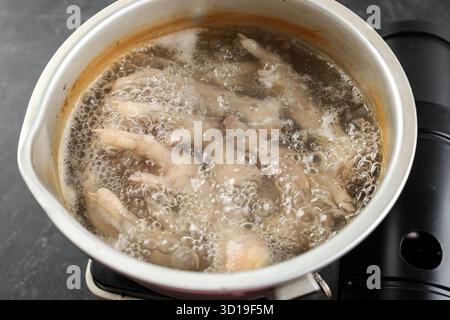 Kochende Hähnchenfüße in einer Aluminiumpfanne, Schritt für Schritt kochen in der Küche. Merebus Ceker Ayam di Panci Stockfoto