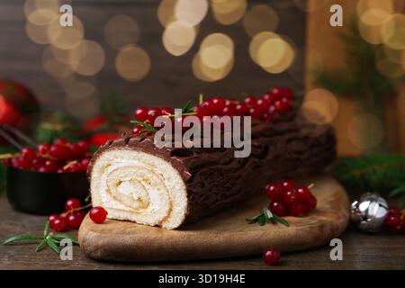 Köstlicher Yule-Stamm (traditioneller Weihnachtskuchen) mit Johannisbeere auf Holztisch, Nahaufnahme Stockfoto