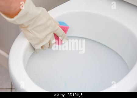 Ein Mann wäscht eine Toilette. Er reinigt die Toilette, um Sauberkeit und Hygiene zu gewährleisten. Stockfoto
