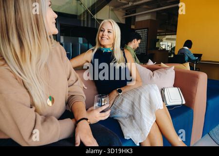 Zwei professionelle Frauen unterhalten sich in einem modernen Büro, fördern Networking und Kameradschaft während einer Pause, während sie von einer entspannten Atmosphäre umgeben sind Stockfoto
