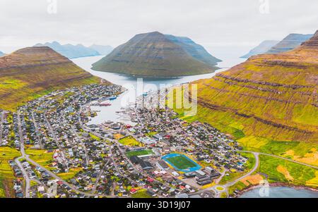 Aus der Vogelperspektive von Klaksvík eingebettet zwischen dramatischen grünen Hügeln und dem klaren blauen Meer, eine lebendige Stadt unter einem weichen, bedeckten Himmel, Klaksvík, Nördliche Inseln, Färöer Inseln. Stockfoto