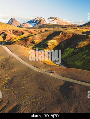 Aus der Vogelperspektive eines einsamen roten Fahrzeugs, das sich entlang einer Straße durch die krasse, kontrastreiche Landschaft von Kerlingarfjöll, Hrunamannahreppur, Island, schlängelt. Stockfoto