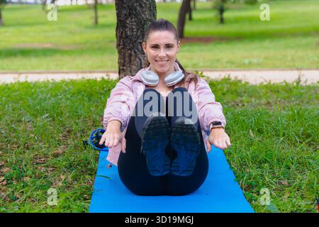 Sportliche Frau beim abs-Workout, die im Park im Freien die Arme auf der Yogamatte hebt Stockfoto