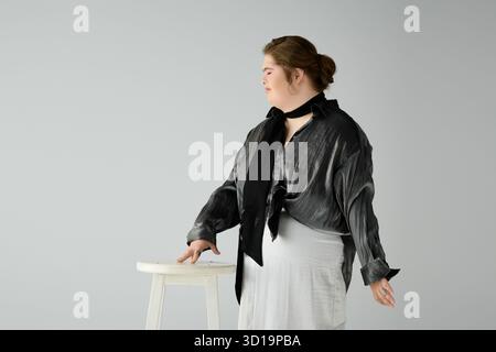 Eine junge Frau mit Down-Syndrom zeigt ihren Stil neben einem weißen Stuhl. Stockfoto