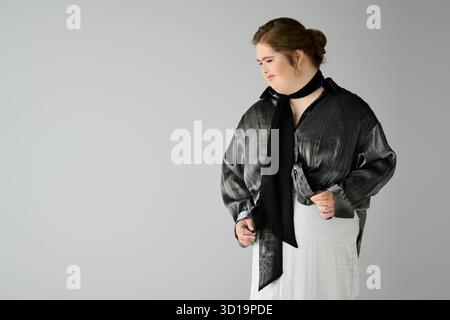Eine junge Frau mit Down-Syndrom zeigt ihren Charme, während sie lächelt und ein schickes Outfit trägt. Stockfoto
