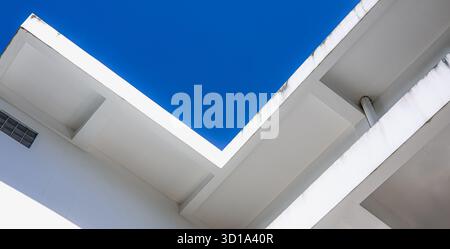 Abstrakte Minimalarchitektur eines modernen weißen Gebäudes mit klaren geometrischen Linien und hellblauem Himmel, die Einfachheit, Struktur und zeitgenössisch zeigt Stockfoto