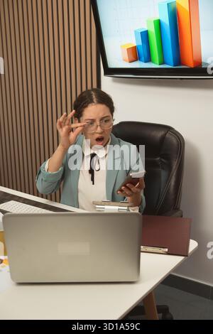 Eine überraschte Geschäftsfrau sieht negative Finanzdaten am Telefon in einem modernen Büro Stockfoto