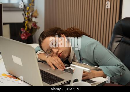 Eine junge Frau, die an ihrem Schreibtisch im Büro schläft, erlebt Burnout und Erschöpfung von der Arbeit Stockfoto