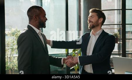 Zwei multiethnische Männer Geschäftsleute Geschäftsteam in Firmensitzung Begrüßung Handschütteln Gespräch diverser kaukasischer Geschäftsmann Stockfoto