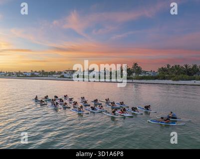 Aus der Vogelperspektive sehen Sie Paddelboarder, die Yoga auf dem ruhigen Meer üben, vor dem Hintergrund der leuchtenden Sonnenuntergänge und der fernen Küste, Progreso, Yucatan, Mexiko. Stockfoto