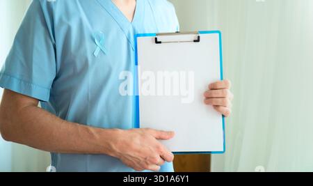 Männlicher Arzt in Uniform mit blauem Band Symbol des Prostatakrebs Bewusstsein halten Clipboard mit leerem Papier für Notizen und Erinnerungen im November. Horizontales Banner Stockfoto