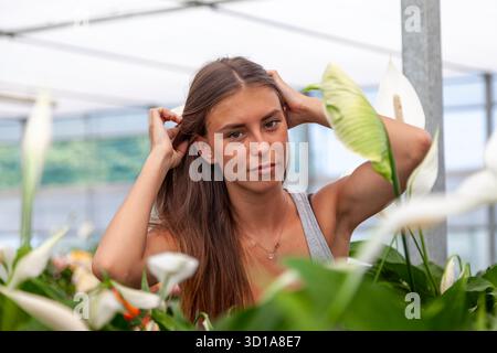 Eine junge Frau posiert beiläufig, umgeben von Lilienpflanzen, natürliches Licht im Gesicht Stockfoto