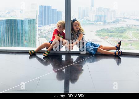 Lustige Kinder haben einen Panoramablick auf Ho Chi Minh City von der Aussichtsplattform des modernen Wolkenkratzers. Urbaner Lebensstil, reisen mit Kindern Stockfoto