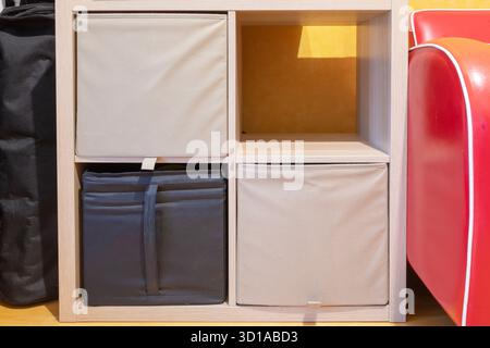 Holzregal mit Textilkästen zur Aufbewahrung. Eine Schachtel ist schwarz und eine andere ist beige. Eine leere Stelle im Regal Stockfoto