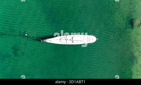 Aus der Vogelperspektive einer einsamen weißen Yacht liegt inmitten des smaragdgrünen Wassers, dessen Reflexion wie eine Fata Morgana schimmert, Sydney, New South Wales, Australien. Stockfoto