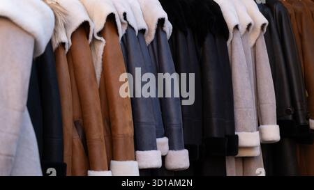 Eine Reihe stilvoller Lammfell- und Ledermäntel in verschiedenen Farben hängt an einem Regal. Das Bild zeigt warme Winteroberbekleidung aus natürlichen Materialien, i Stockfoto