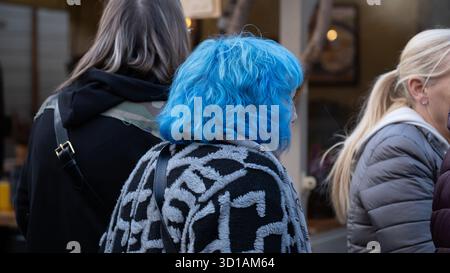 Eine Gruppe von Menschen, die auf einer Straße der Stadt stehen, mit einer Frau mit hellblauen Haaren und gemusterter Kleidung im Fokus. Gefangen genommen in Krakau, Polen, Octo Stockfoto