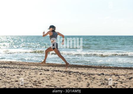 Athleten laufen auf Sandstränden an der Küste, die Teilnehmer beschleunigen die feuchte Küste entlang, während die Wellen abstürzen und das Sonnenlicht die Szene erleuchtet Stockfoto