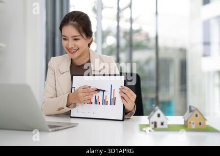 Lächelnder asiatischer Erwachsenenagent erklärt Wohnungstrends auf einem Balkendiagramm während eines virtuellen Meetings mit Laptop, der Immobilieninvestitionen zeigt Stockfoto