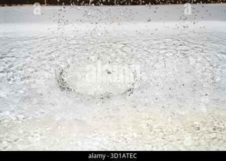 Saubere Wassertropfen aus dem Duschkopf fallen auf den weißen Fliesenboden, was zu einer Überschwemmung im Badezimmer führte, da der Duschabfluss verstopft war. Stockfoto