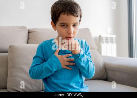 Kind, das zu Hause auf dem Sofa sitzt und die Hand auf der Brust hält. Männer mit Asthmaanfall, Atembeschwerden, starken Schmerzen oder Dyspnoe Stockfoto