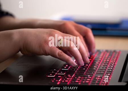 Nahaufnahme einer Geschäftsfrau, die spät am Tippen auf einer blauen Hinterleuchtung arbeitet, die auf der Tastatur des Laptops hinterleuchtet ist. Anonymität im Internet kann in puncto Vorteile bieten Stockfoto
