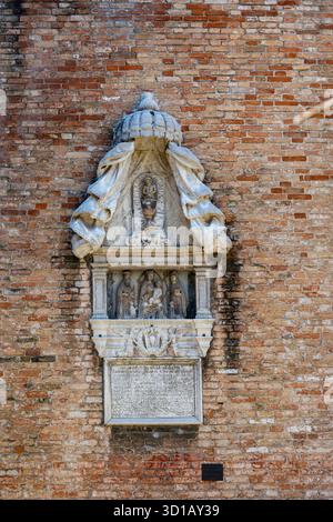 Religiöse Steinreliefskulptur auf venezianischer Ziegelmauer. Kompliziertes Marmorrelief mit heiligen christlichen Figuren, die auf einer alten Ziegelmauer montiert sind Stockfoto