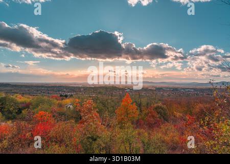 Ein wunderschöner Herbsttag mit einer hellen Sonne, die durch die Wolken scheint. Der Himmel ist blau und die Bäume sind mit Blättern bedeckt Stockfoto