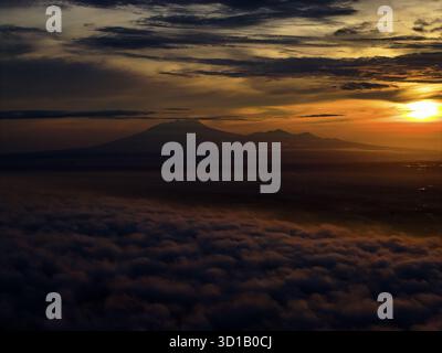 Aus der Vogelperspektive auf eine lawu-Bergkette, die bei Sonnenaufgang durch eine dicke Wolkendecke durchsticht und einen warmen goldenen Glanz über den Horizont wirft, Karanganyar Regency, Zentral-Java, Indonesien. Stockfoto